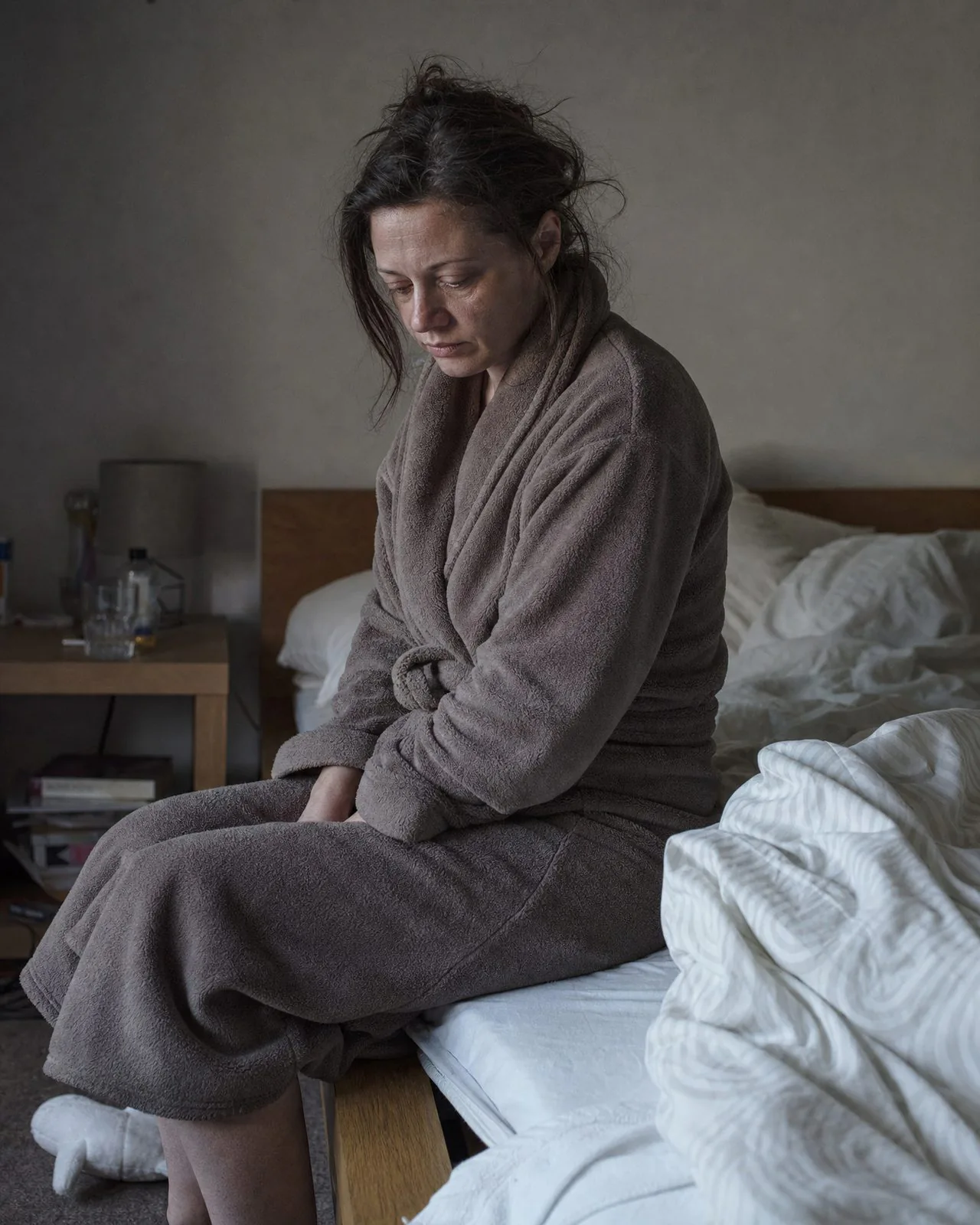 Élodie assise au bord d'un lit, épaules basses, le regard au sol