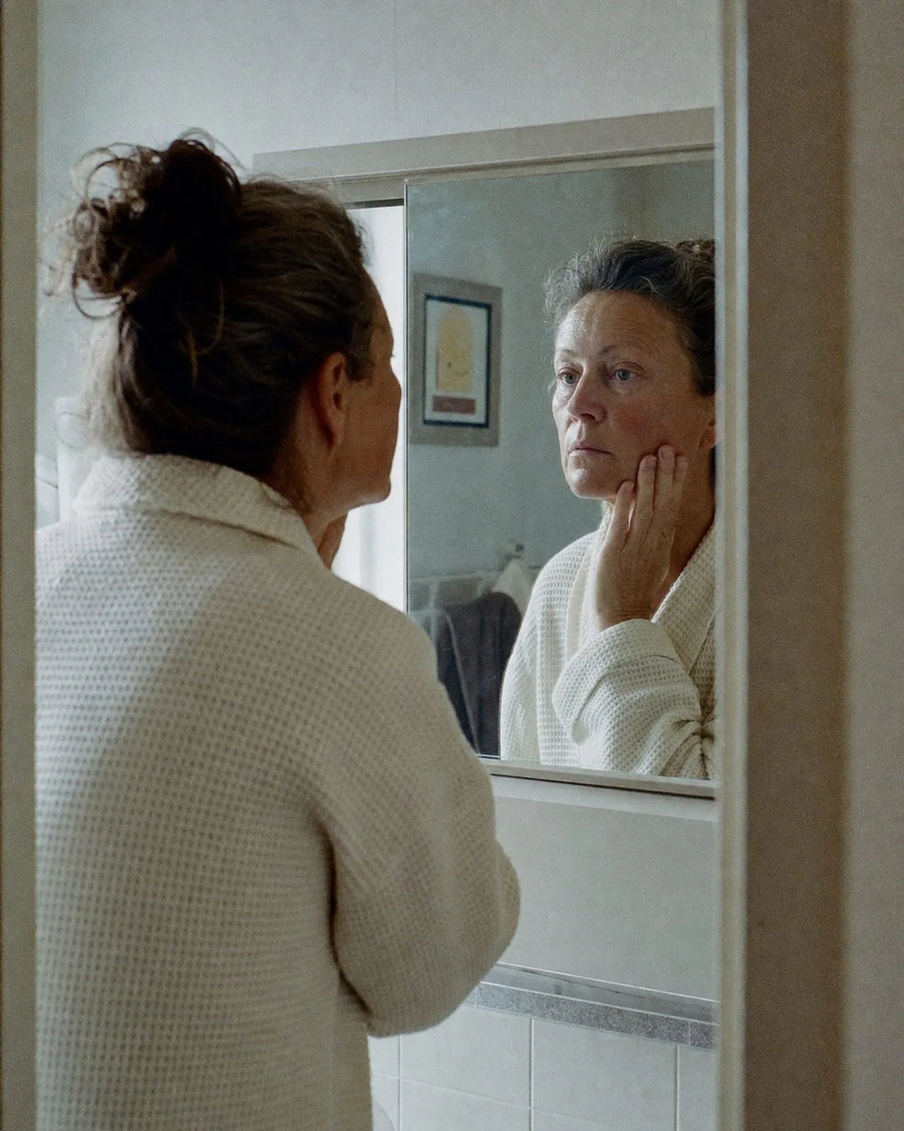 Véronique se regarde dans un miroir, une main sur la joue