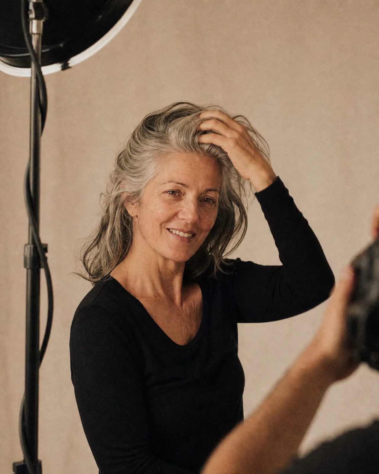 Véronique devant l'objectif, repoussant ses cheveux gris en souriant